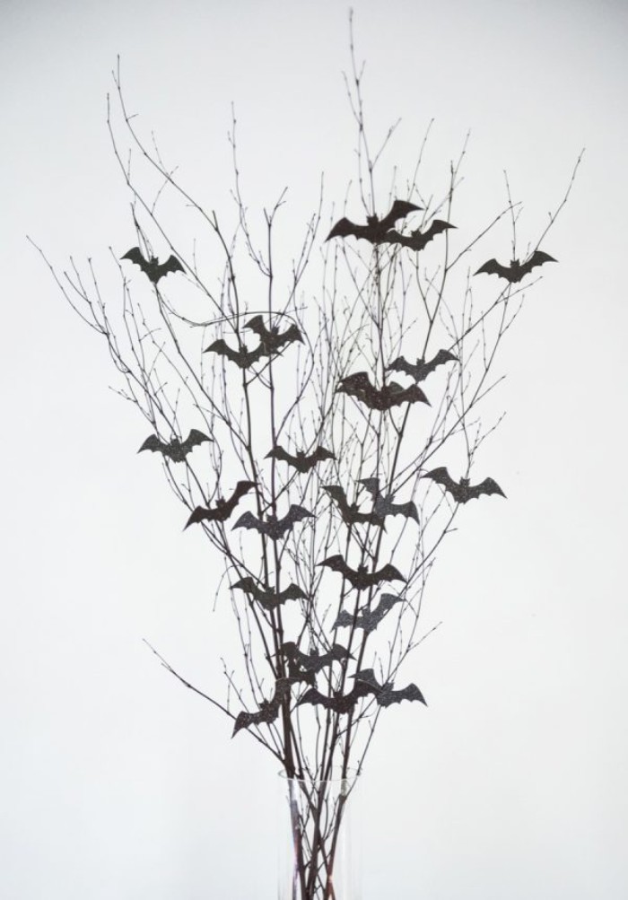 thin dried branches, decorated with small bath shapes, cut out from black card, in a clear glass vase, on a white background