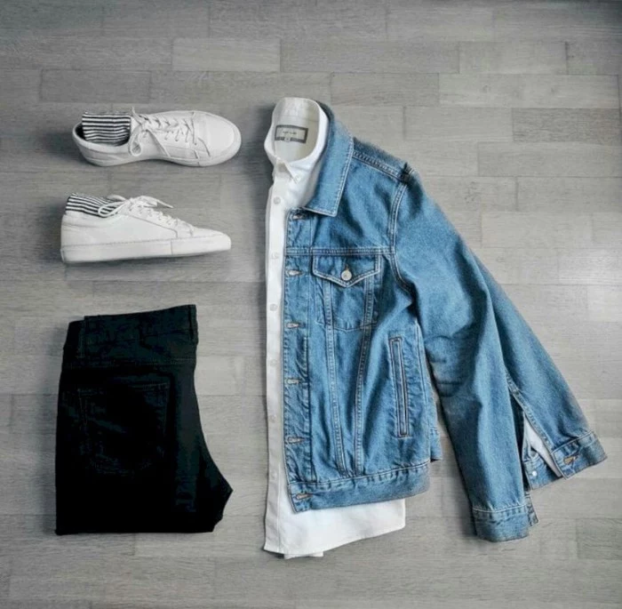 sneakers in white, with striped socks, palced near a folded, blue denim jacket, wardrobe essentials for guys, a white shirt, and a pair of folded black trousers