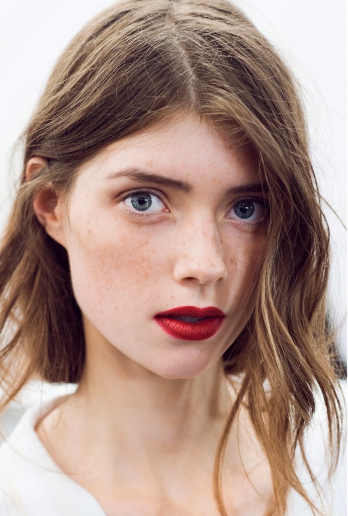 messy light brunette wavy hair, with a middle part, on a pale young woman, with blue eyes and freckles, wearing bright red lipstick