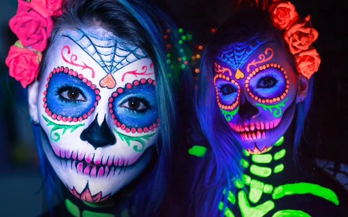 neon colored sugar skull face paint, with glow-in-the-dark details, halloween face paint ideas for adults, worn by a young woman, with dark eyes