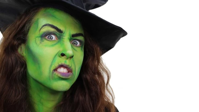 classic witch face paint, brunette woman with long curly hair, wearing green paint on her face, and a black witch's hat