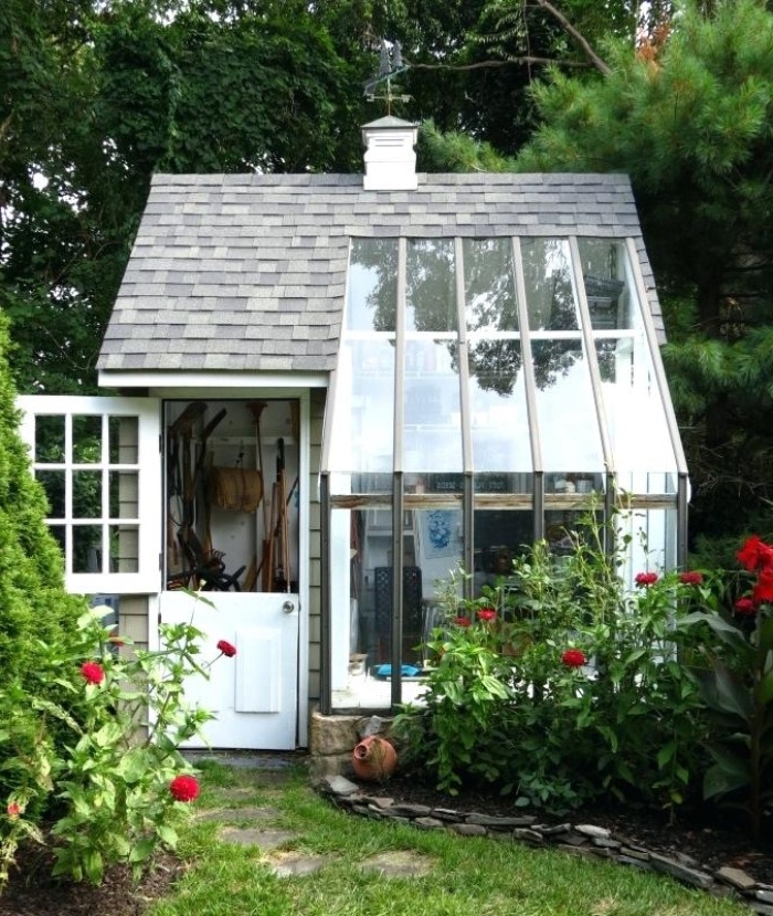 large glass panels, on an orangery style shed, with grey tiled roof, and a partially open door, revealing various tools inside 