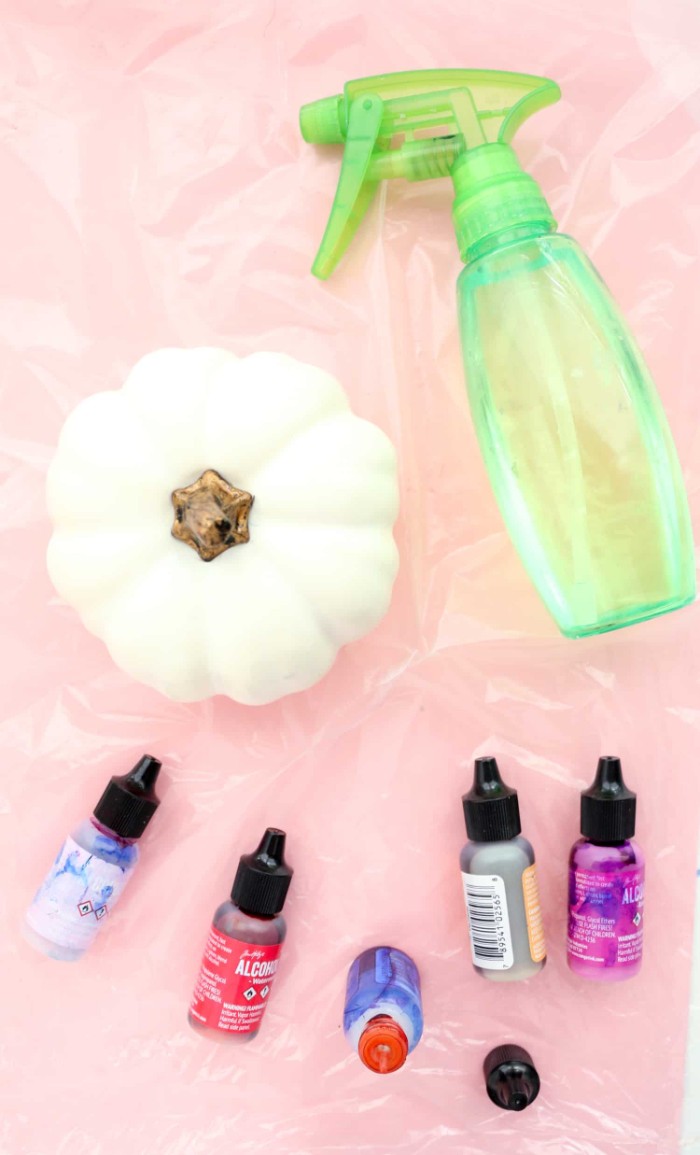 clear green plastic spray bottle, near a small white fake pumpkin, and five bottles of paint, in different colors, halloween pumpkin decorations