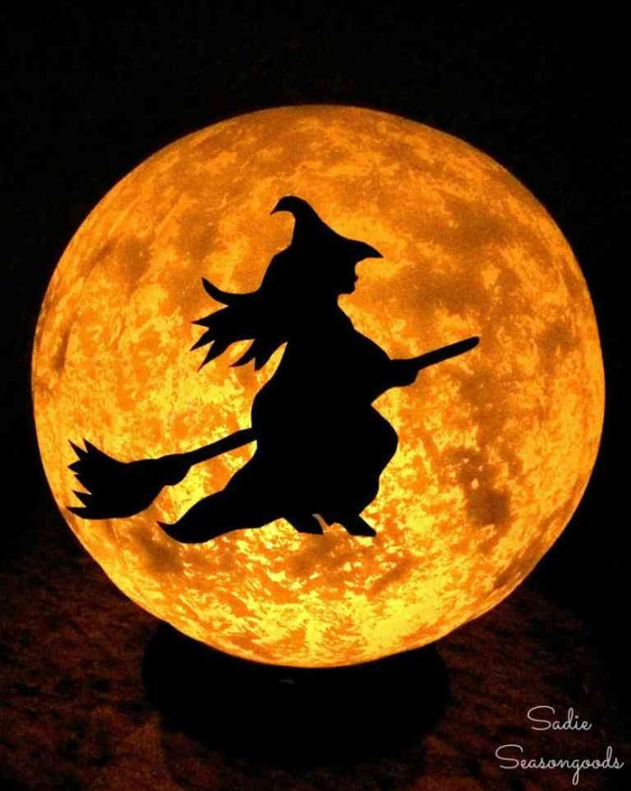 halloween witch decorations, black outline of a witch, flying on a broomstick, stuck to a glowing, moon-like beige lamp