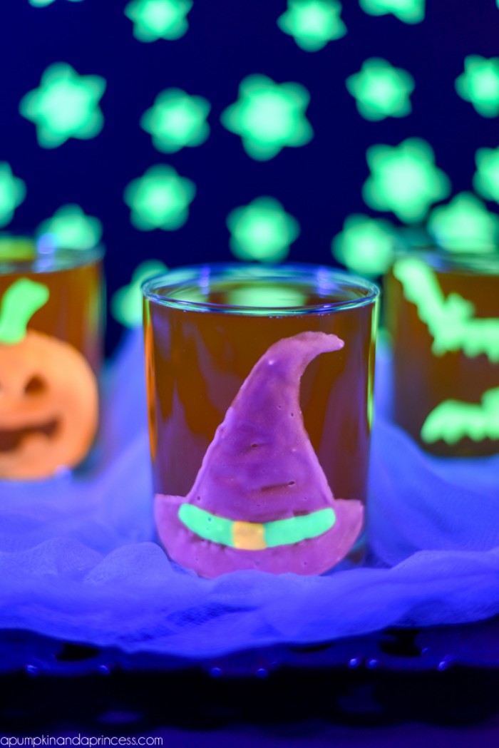 purple witch's hat, glow-in-the-dark sticker, with neon green, and orange details, stuck on a glass, halloween party decoration ideas, more glowing shapes in the background, bats and stars