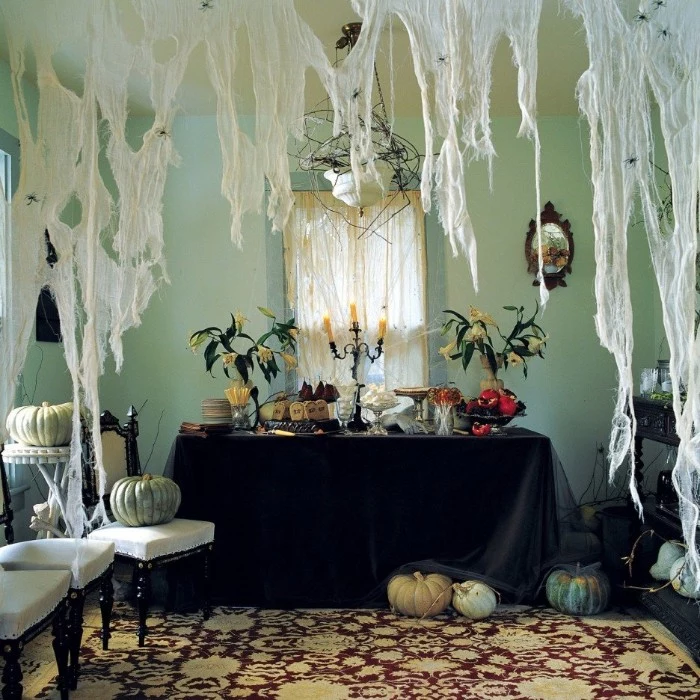 haunted house decorations, huge fake cobwebs, hanging over a table, with a black tablecloth, two vases with wilted flowers, and an antique candlestick