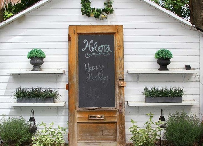 blackboard attached to the vintage wooden door, of a white shed, decorated with several potted plants, garden shed ideas