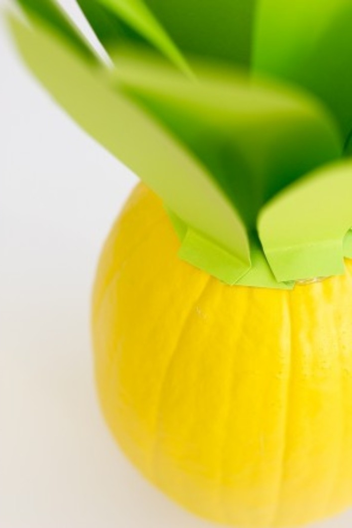 how to decorate your room, close up high angle shot, of a pumpkin, spray-painted yellow, and decorated with light green, leaf-shaped paper cutouts on top