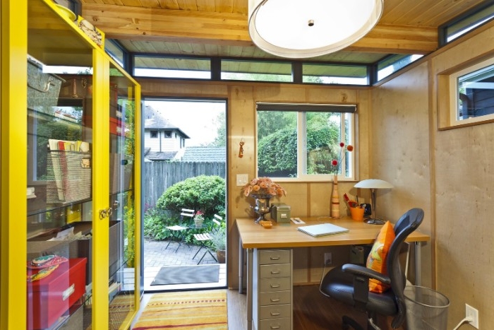 desk and an office chair, inside a small garden shed, containing a yellow cupboard, she shed interiors