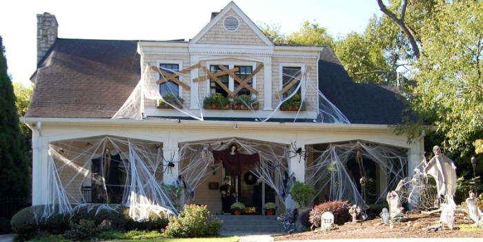 scary outdoor halloween decorations, house covered in fake cobwebs, with boarded windows, huge plastic spiders, and several skeletons in the yard