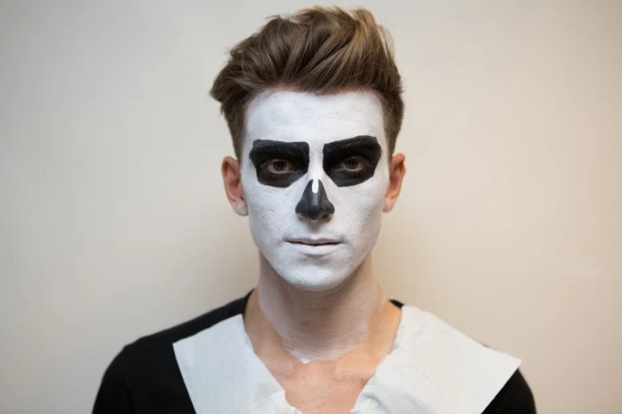 drawing skeleton features, with black and white paint, on the face of a young man, with brunette hair