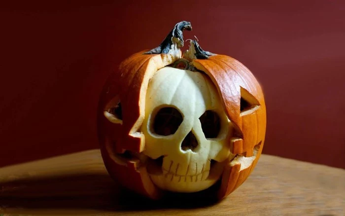 carved pumpkin with two layers, orange jack-o-lantern, cut to reveal a smaller, white pumpkin within, carved to look like a skull, skeleton pumpkin