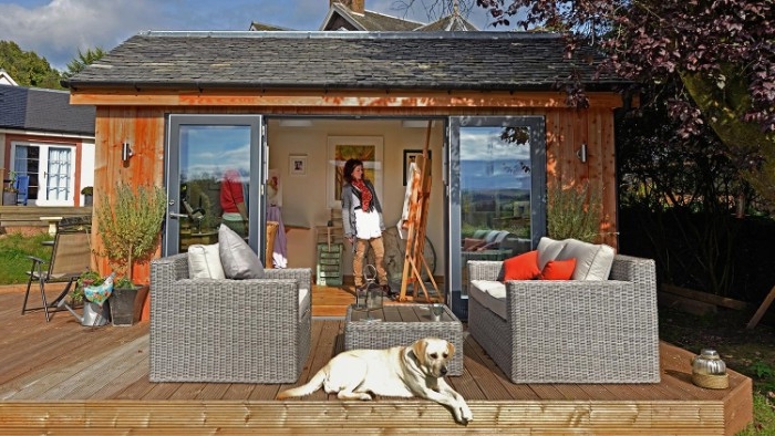 rattan garden furniture, and a white dog, in front of a shed with open doors, woman standing next to an easel inside, she shed images 