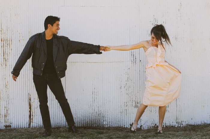 dancing smiling couple, young woman dressed in a pale peach dress, holding the hand of a man, with black clothes, and a black leather jacket, quick halloween costumes, inspired by grease