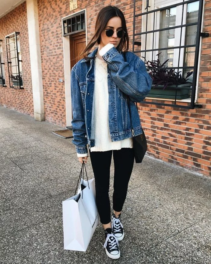 wearing capsule closet items, black leggings and a white blouse, oversized denim jacket, and classic converse sneakers, on a young brunette woman, wearing sunglasses