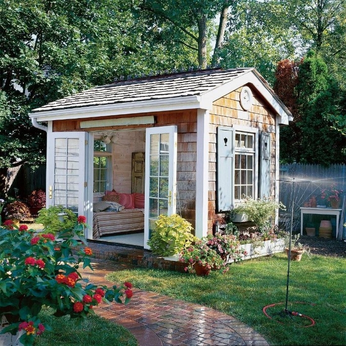 tiled roof on a wooden shed, with open double doors, and windows with wooden shutters, shed ideas, garden with sprinkler, and many plants