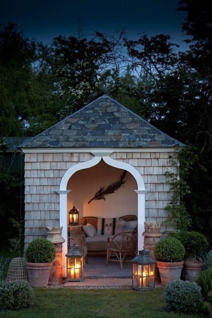 gazebo style shed, containing a sofa, a chair and a lantern, she shed images, inside a garden, with potted plants, and two lit lanterns