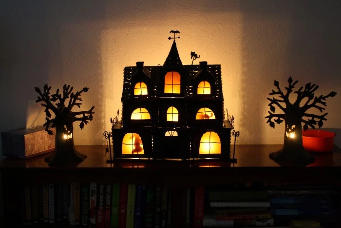 miniature haunted house decorations, a black house illuminated from within, and two small tree figurines with faces