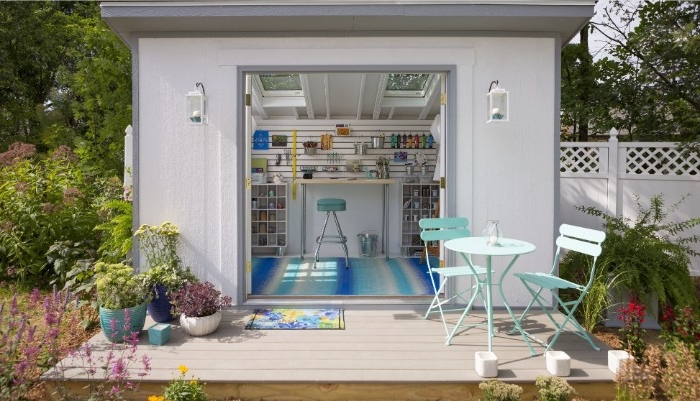 she shed interiors, small white structure with open doors revealing a striped blue and white rug, a blue stool, and various shelves with tools