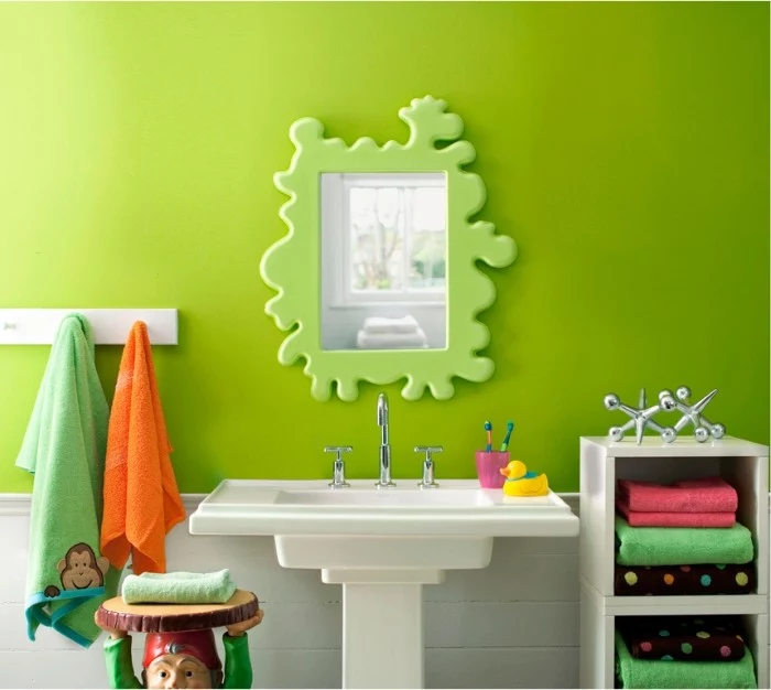 decorative mirror in a splatter-like, pale green frame, mounted on a lime green wall, bathroom paint colors, white sink and cupboard, and colorful decorative items