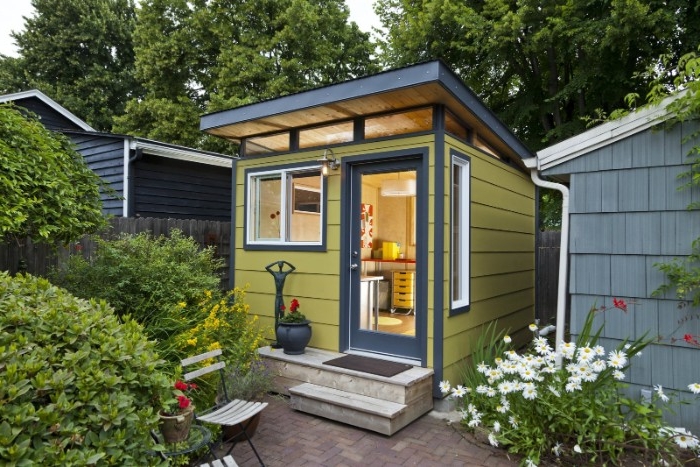 grey and yellow cube-like shed, surrounded by other similar structures, shed ideas, inside a garden with trees and shrubs