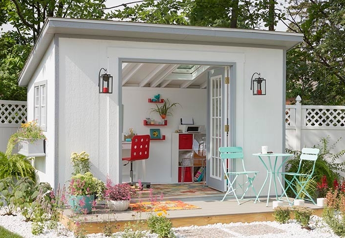 table and two chairs, in front of a white shed, with open doors, revealing a red modern chair, a multicolored rug, and some shelves inside, she shed interiors in red and white