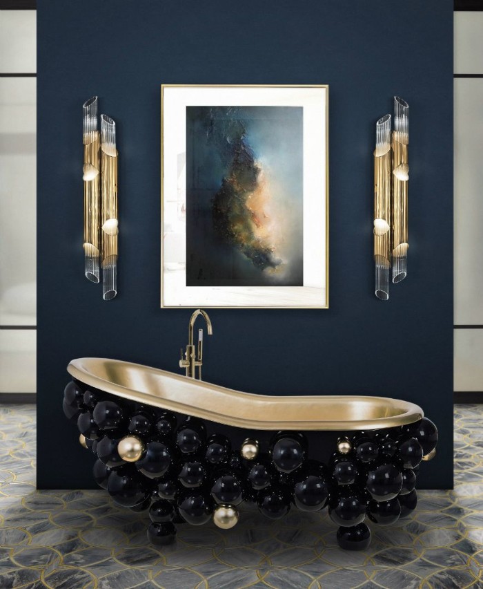 decorative spheres in black and gold, decorating a vintage-style bathtub, near a navy blue wall, decorated with a painting, and two modern lamps, bathroom picture ideas, stone tiled floor