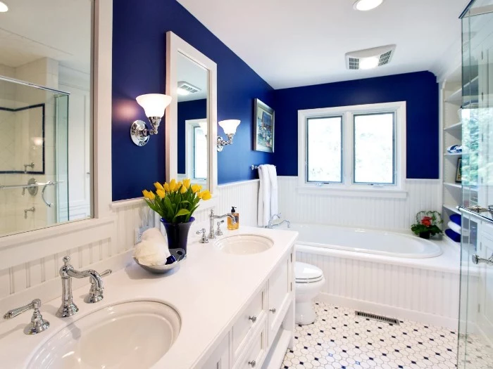 two mirrors in white frames, on the navy wall of a bathroom, with white wooden paneling, bathroom paint colors, black and white, mosaic tiled floor