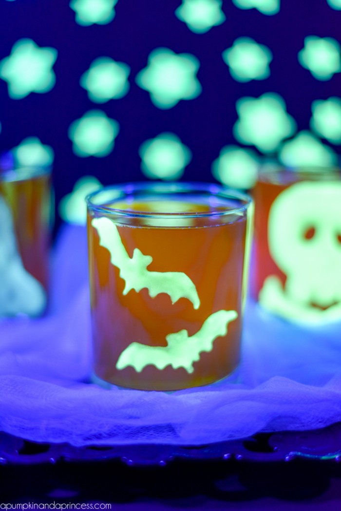 a pair of bats, painted in a glow-in-the-dark neon green color, and stuck on a small orange glass, halloween party decoration ideas, glowing stars in the background