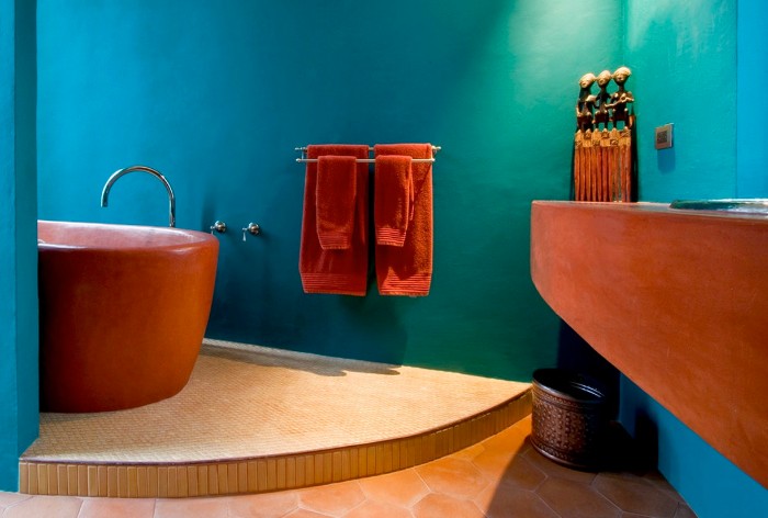 terracotta bathtub and sink, in a room with a beige stone tiled floor, and ocean blue walls, two sets of orange towels