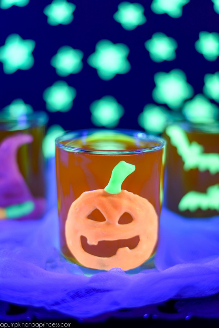 glow-in-the-dark pumpkin sticker, in orange and green, decorating a small orange glass, halloween decorations, more glowing shapes in the background