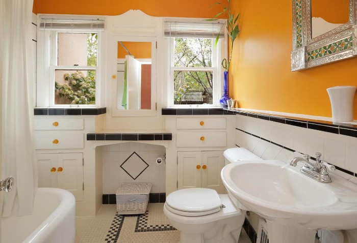 white bathroom furniture, in a room with orange walls, best paint for bathrooms, two windows and a mirror, bathtub a toilet and a sink