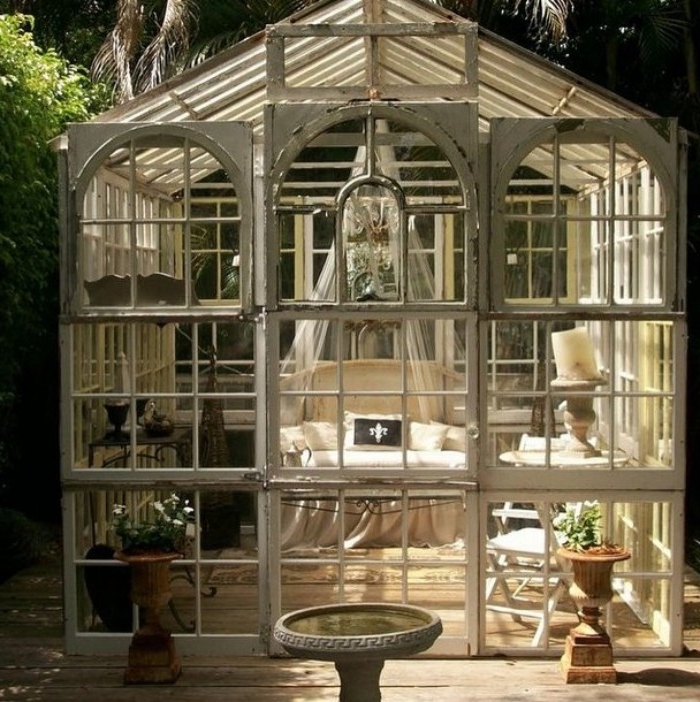 antique greenhouse style shed, with lots of glass panels, and white frames, containing a small cream sofa, with a sheer white baldachin