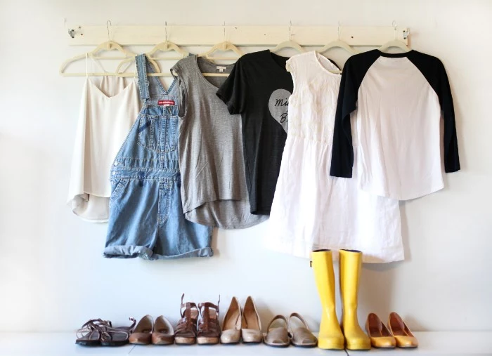 dungarees made of blue denim, a cami top, two t-shirts, a jumper and a white lace mini dress, capsule wardrobe planner, hanging over six pairs of shoes, and a pair of rubber yellow boots
