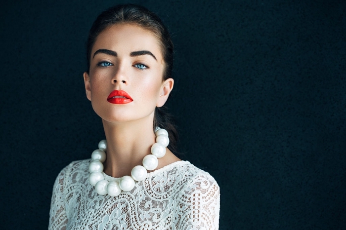 holiday makeup 2017, young blue-eyed woman, dressed in a white lace top, with an oversized pearl necklace, and bright red lipstick