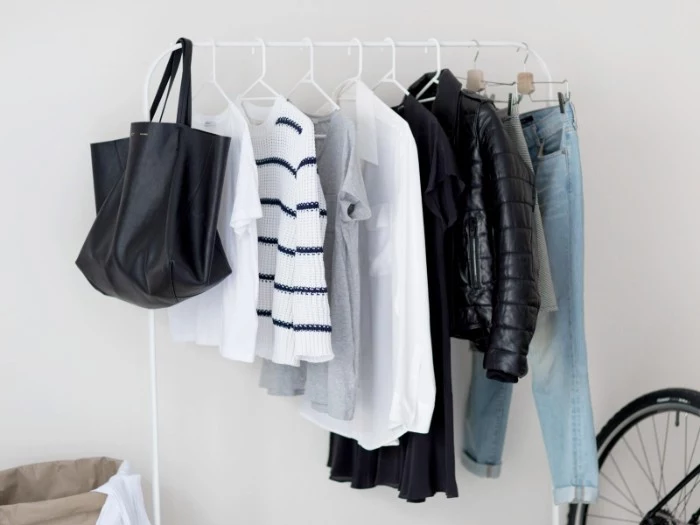 light blue jeans, black winter jacket, white shirt and grey t-shirt, striped jumper and white t-shirt, and a black tote bag, hanging on a clothes rack, capsule wardrobe