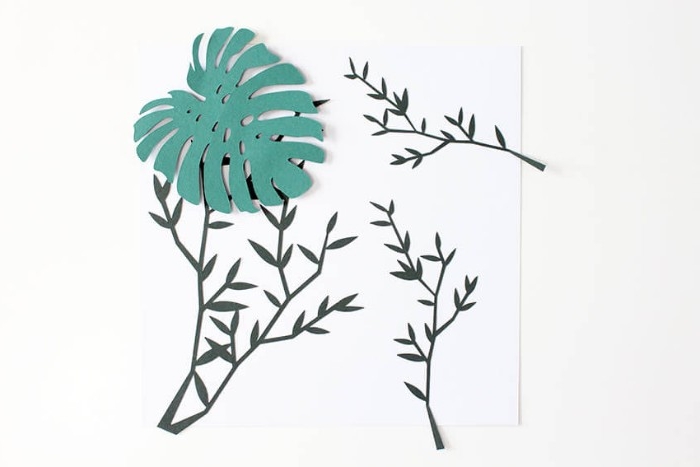 creating a 3D paper collage, diy bedroom décor, sticking a palm leaf-shaped, green paper cutout, on top of a few branch-like paper shapes, using adhesive strips
