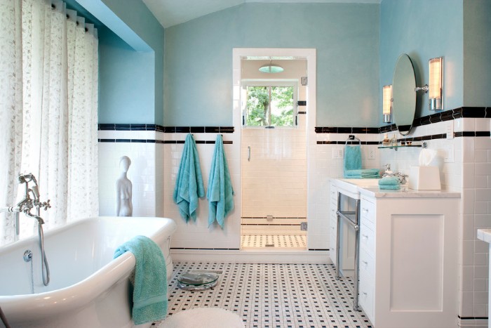 white shower curtains, with a pale pattern, near a vintage style white bathtub, in a room with pale blue walls, half-covered with white subway tiles, featuring black details