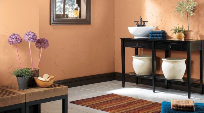 textured walls in peach pink, inside a bathroom, with black and brown furniture, a small window, and several indoor plants