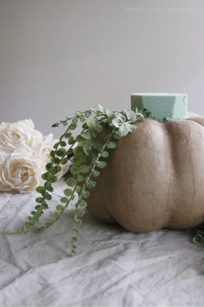 papier mache pumpkin in beige, dollar store crafts, with a mint green florist sponge on top, decorated with plastic green plants