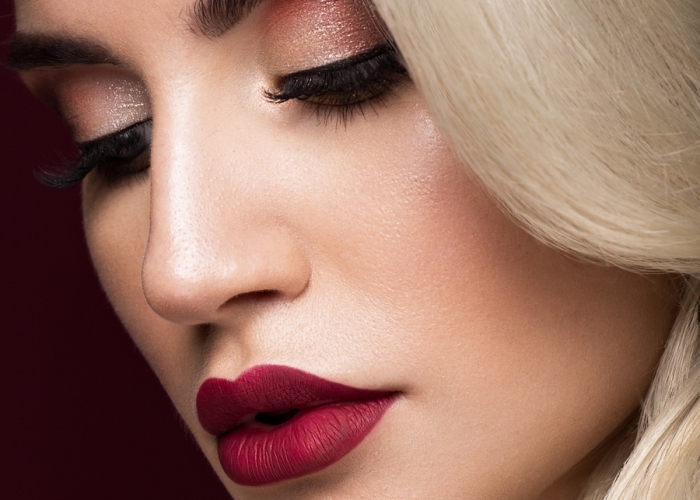 burgundy red lipstick, shimmering pale brown eye shadow, and long fake lashes, christmas makeup ideas, worn by a platinum blonde woman