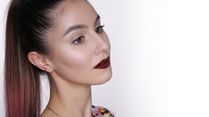 brown-eyed woman, with a long brunette ponytail, and subtle pink highlights, wearing dark red lipstick, and black mascara