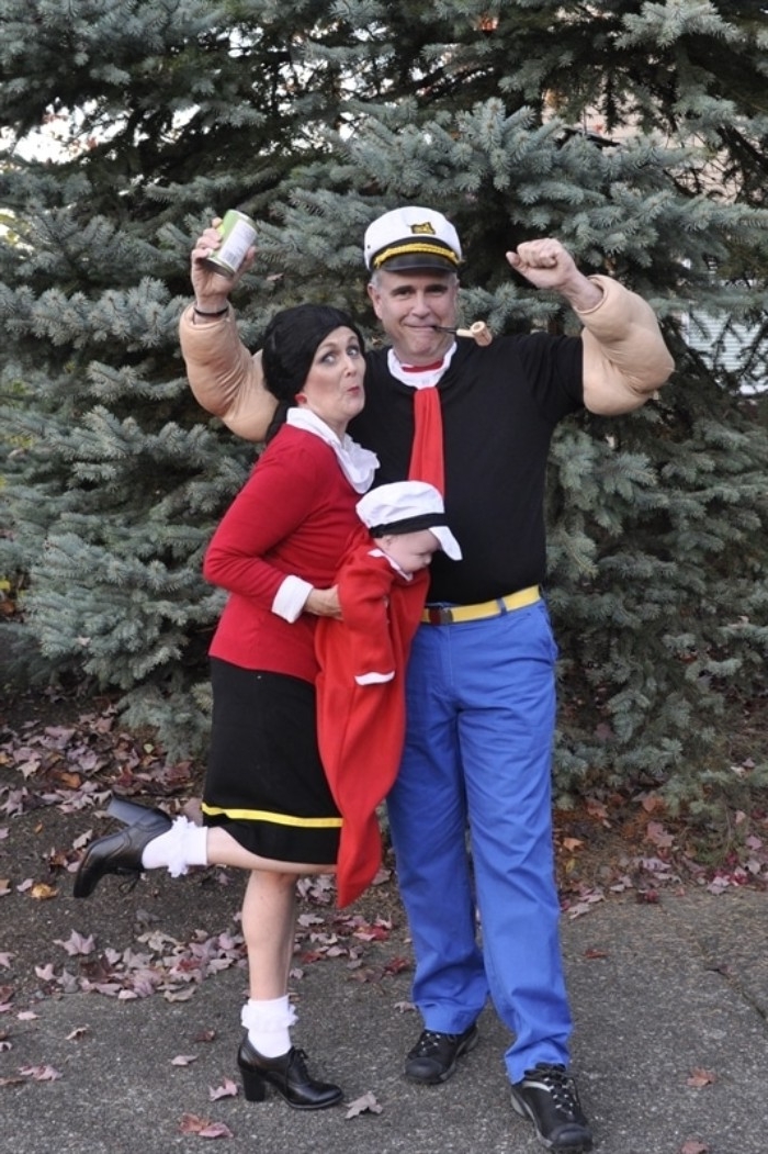 olive oyl and popeye the sailor, duo halloween costumes, man dressed like a captain, with a pipe and a can of spinach, woman in red jumper, and black skirt, holding a baby