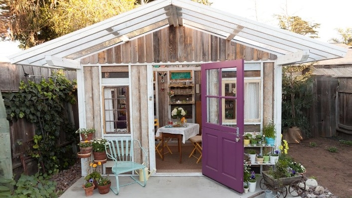 panels made of glass, and white frames, making up the roof, of a wooden shed, with several windows, and an open purple door