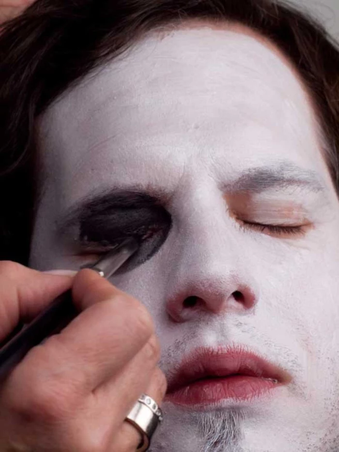 black eye shadow, applied onto the eyelid of a young man, wearing white paint on his face, clown face paint, step by step tutorial