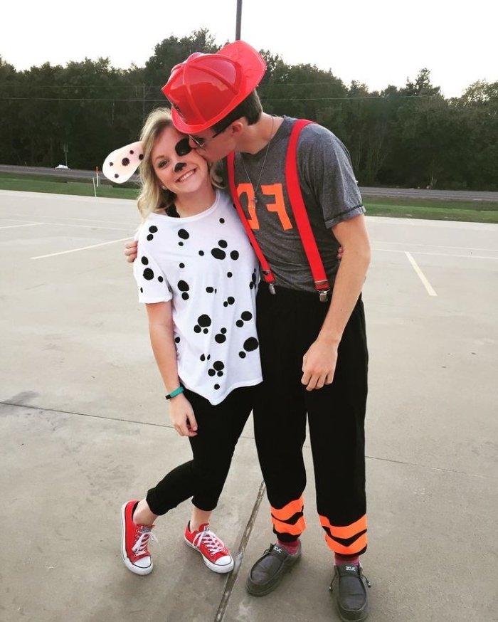 firefighter and dalmatian, funny couple halloween costumes, man with red hard hat, kissing the cheek of a young woman, in a white t-shirt with black spots, wearing face paint and puppy ears