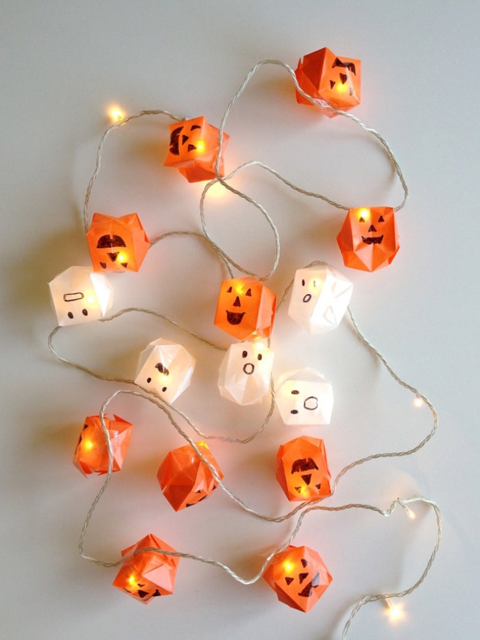 string lights decorated with paper origami shapes, in orange and white, made to look like jack-o-lanterns, and little ghosts