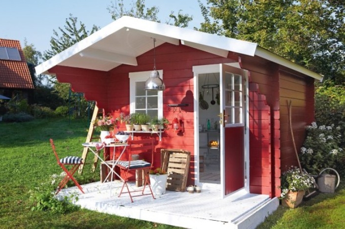 shed ideas, red and white structure, with an open door, and a small window, garden table and two chairs, standing in front of it