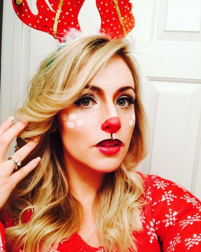 festive makeup for chistmas, reindeer face paint, with a red nose, worn by a blonde woman, wearing a red christmas sweater, and a head decoration with antlers