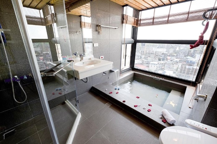 tub with rectangular shape, filled with water, and decorated with scattered rose petals, spa like bathrooms, large window overlooking a city